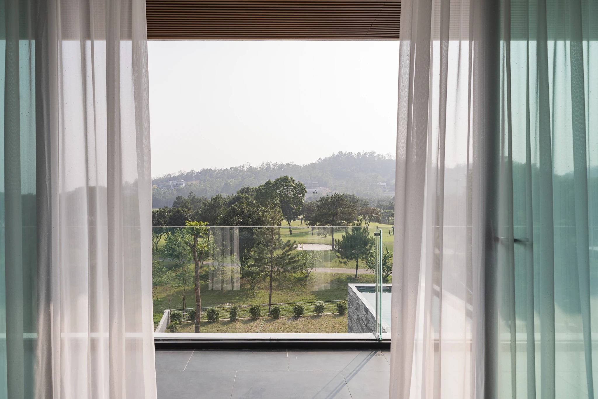 Sáng — view ban công phòng ngủ ra sân golf Tam Đảo qua rèm voan tại Moon Villa C27